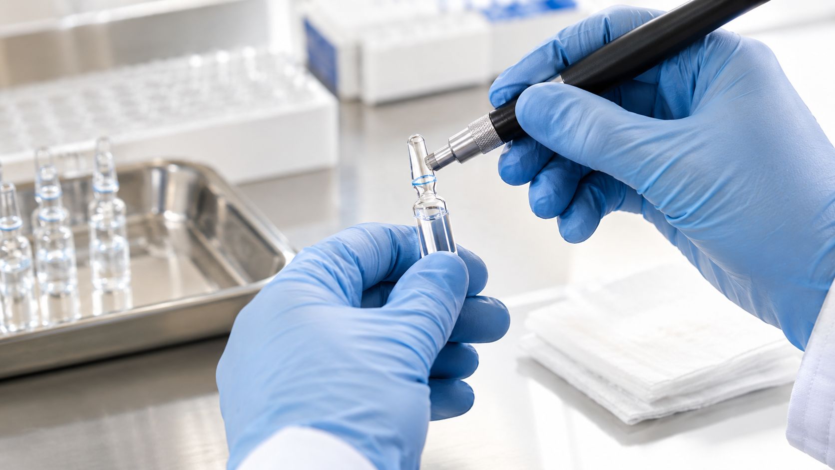 A gloved laboratory technician uses a specialized tool to safely open a glass medical ampule.